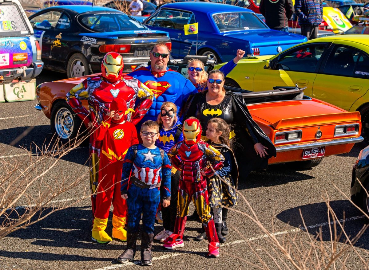 Group of adults & kids dressed up as superheroes standing in front of old cars for the Classis Cruise