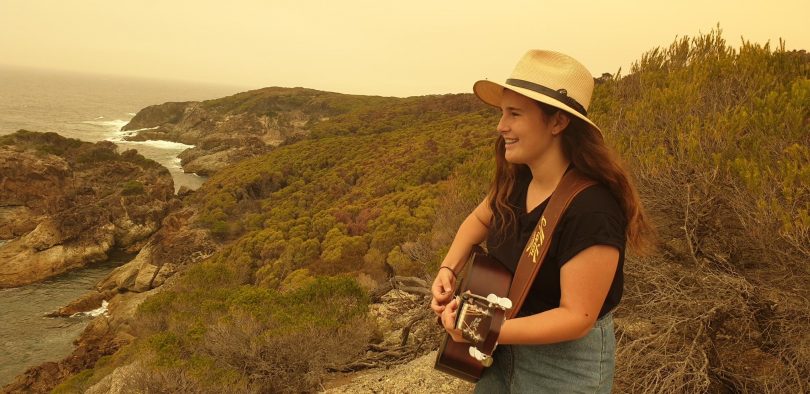 Felicity Dowd playing guitar on cliff.