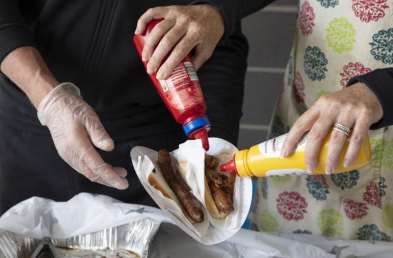 Two people holding sauce bottles at sausage sizzle