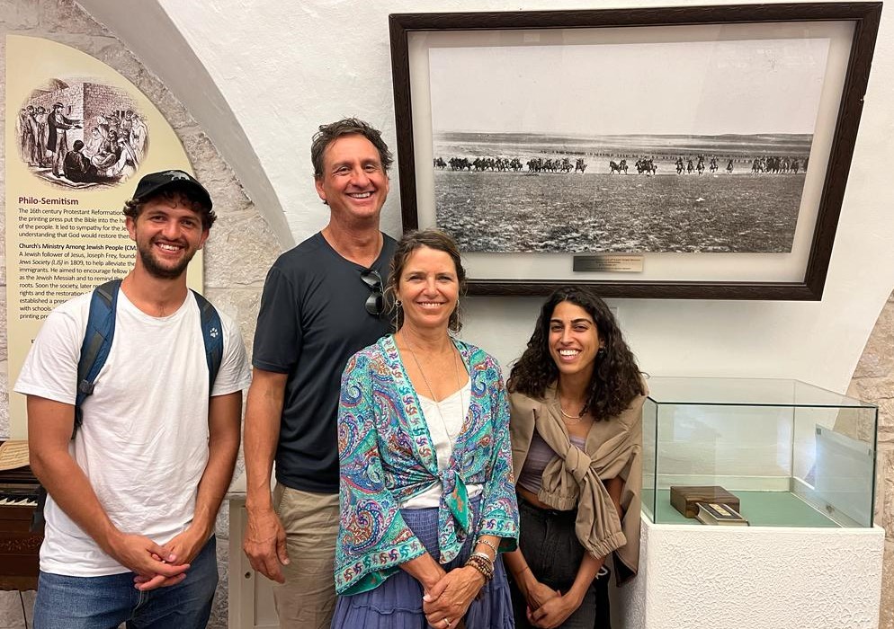 Four people standing in front of a photo of the charge of the Australian Light Horse at Beersheba