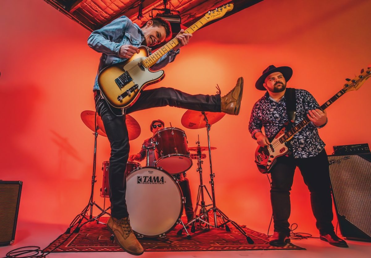 A guitarist jumps in the air as a band plays behind.