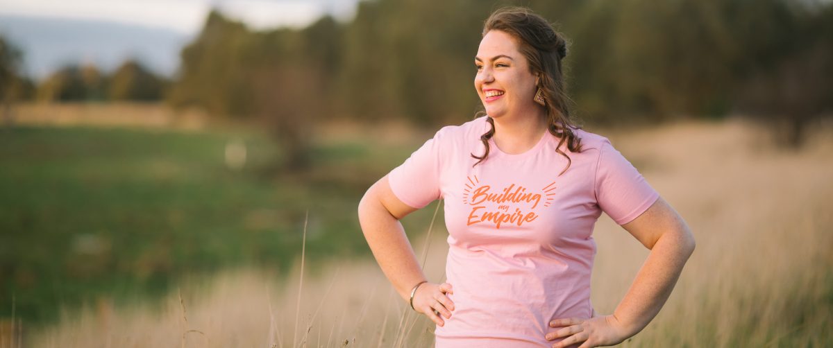 Meredith West smiling and standing in a field wearing a pink tshirt