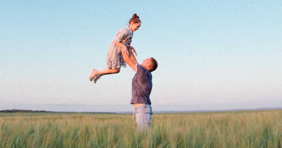 Father holding daughter in the air in field