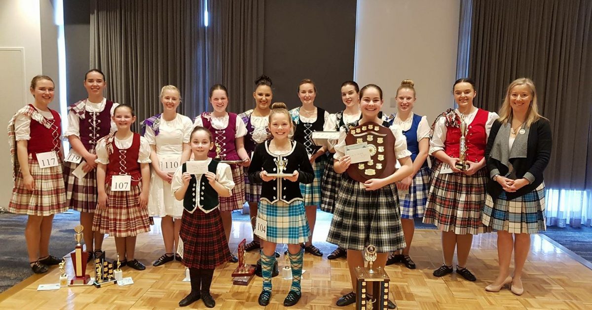 Highland dancers lined up on stage with trophies