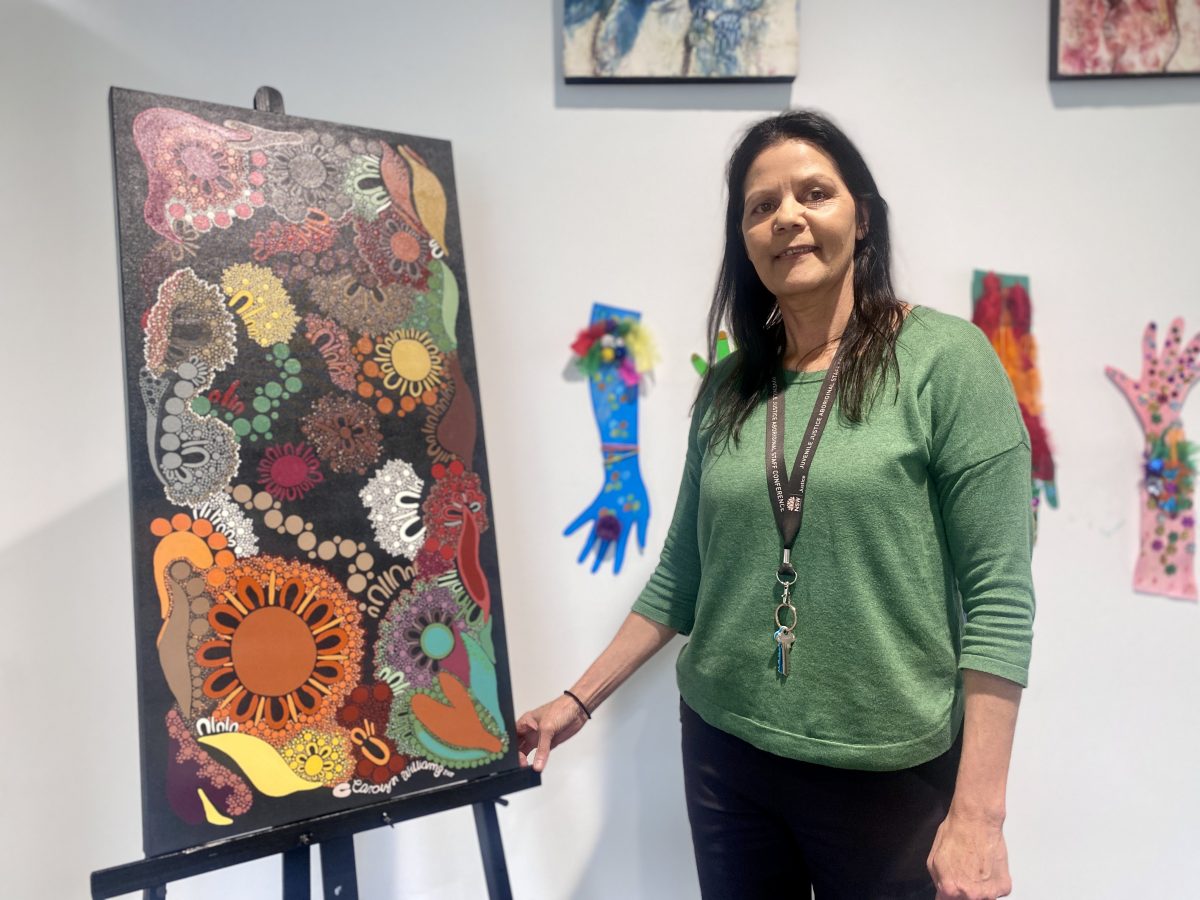 Indigenous artist standing next to her painting