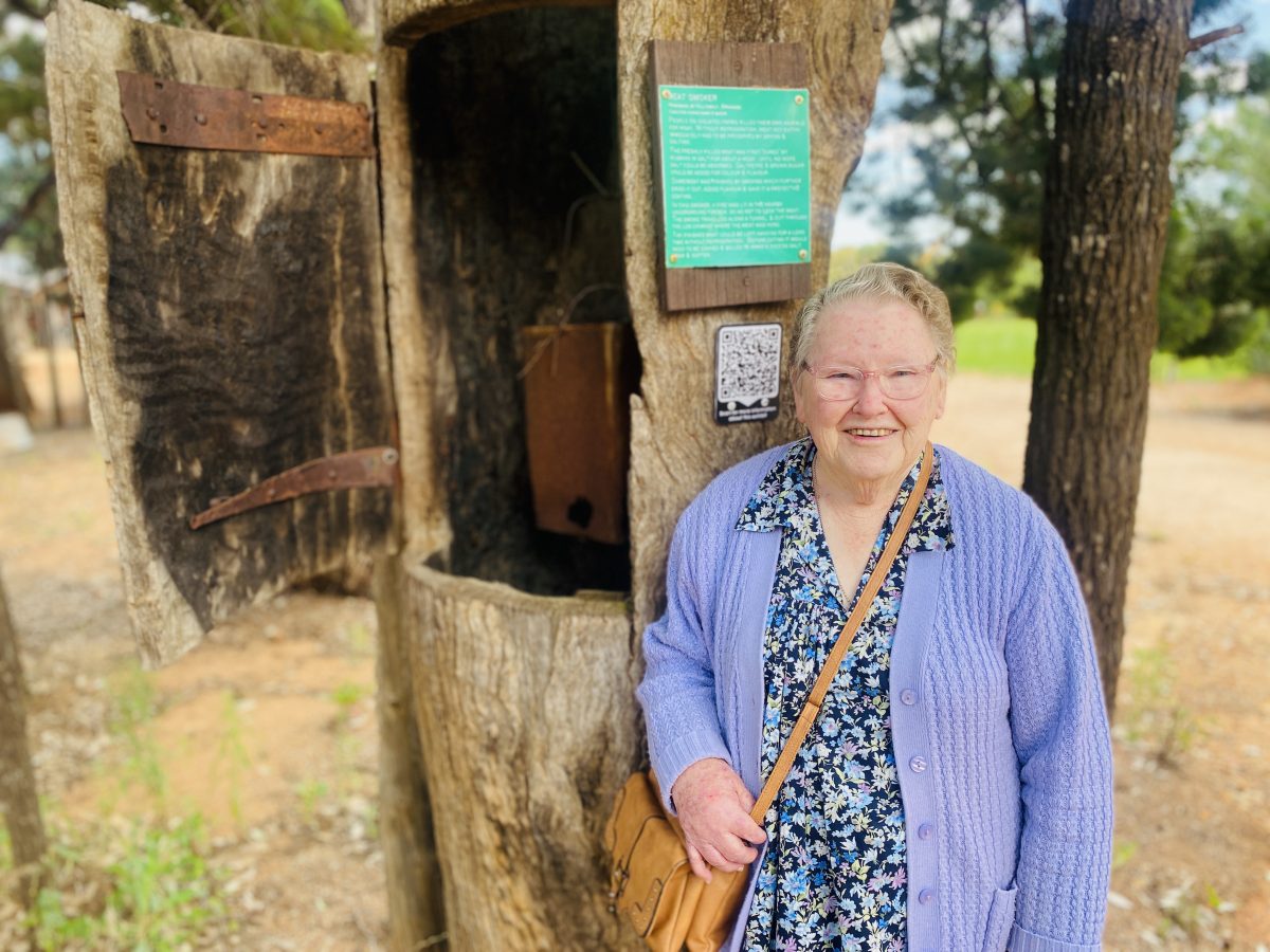Marjory Longford stands next to log smoker 