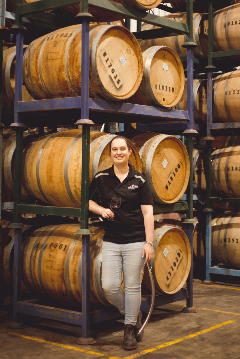 Mel McWilliam standing in front of wine barrels