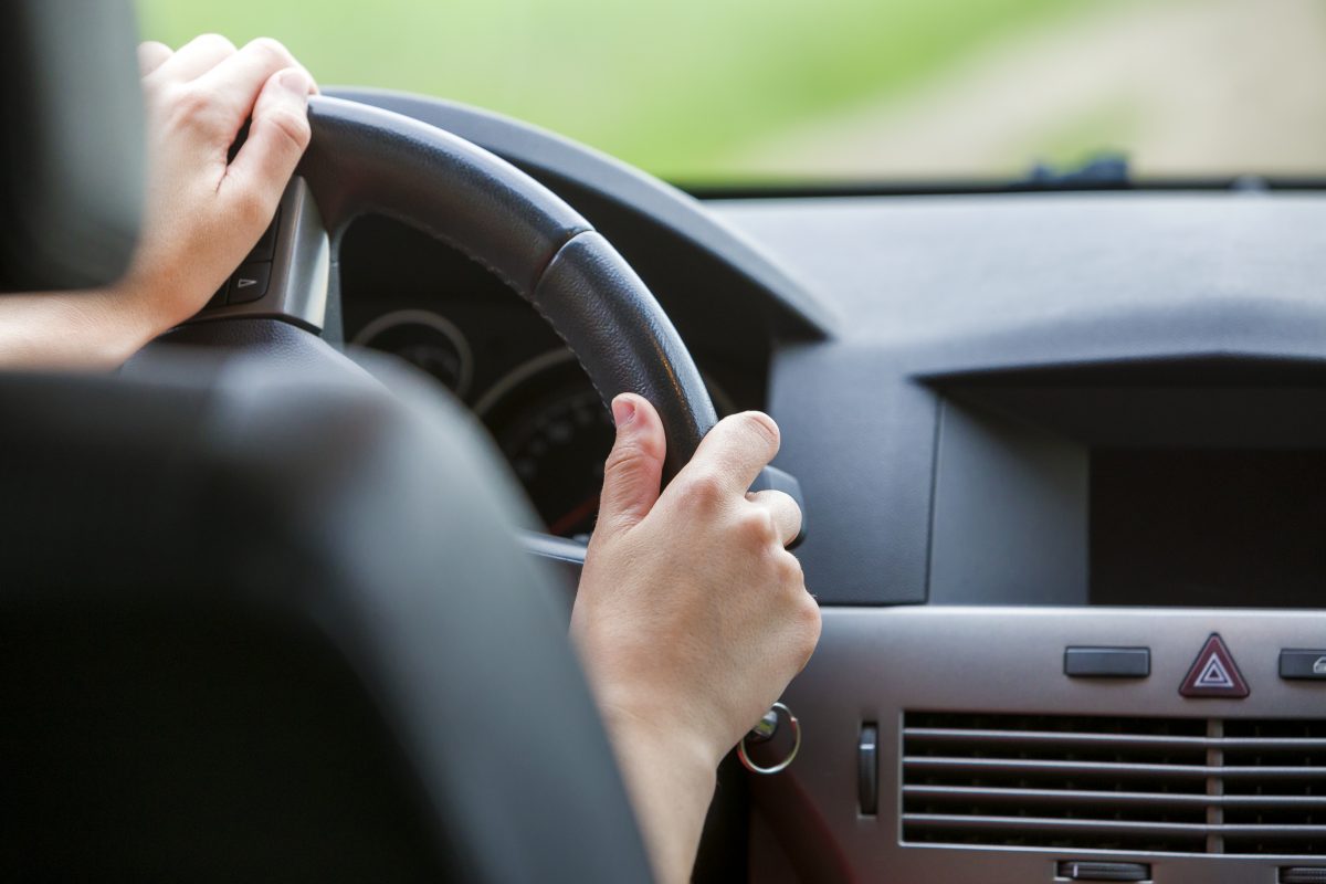 Woman hands on steering wheel driving a car.