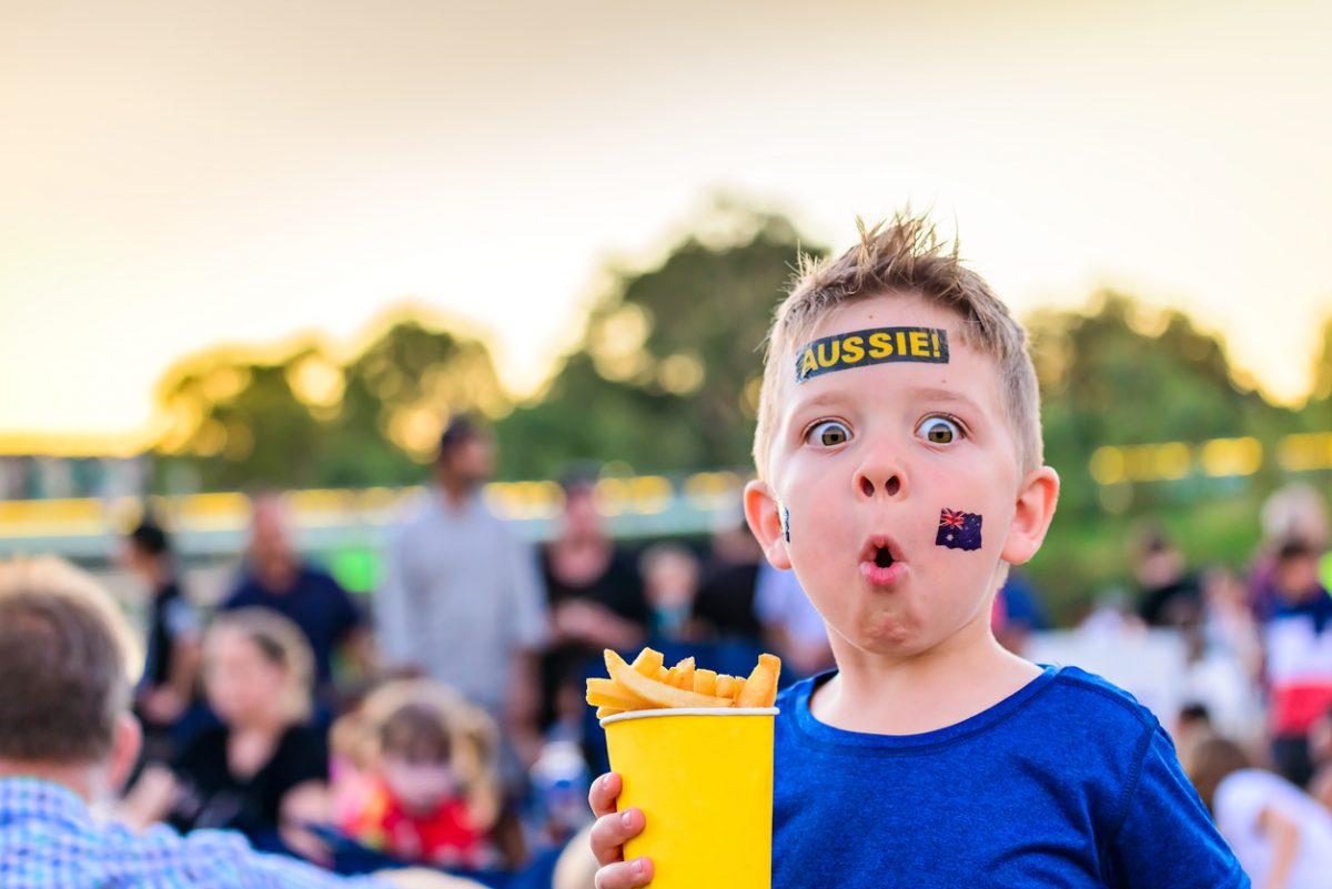 Little boy with Australia flag temporary tattoo on face holding a cup of hot chips