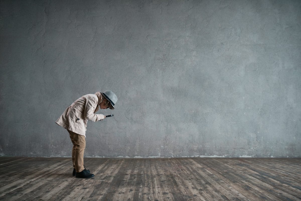 Little boy with a magnifying glass examines the floor of an empty room