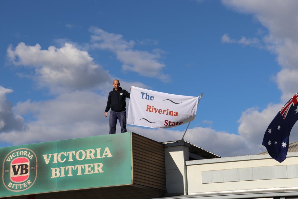 Guy with Riverina state flag on roof next to VB logo 
