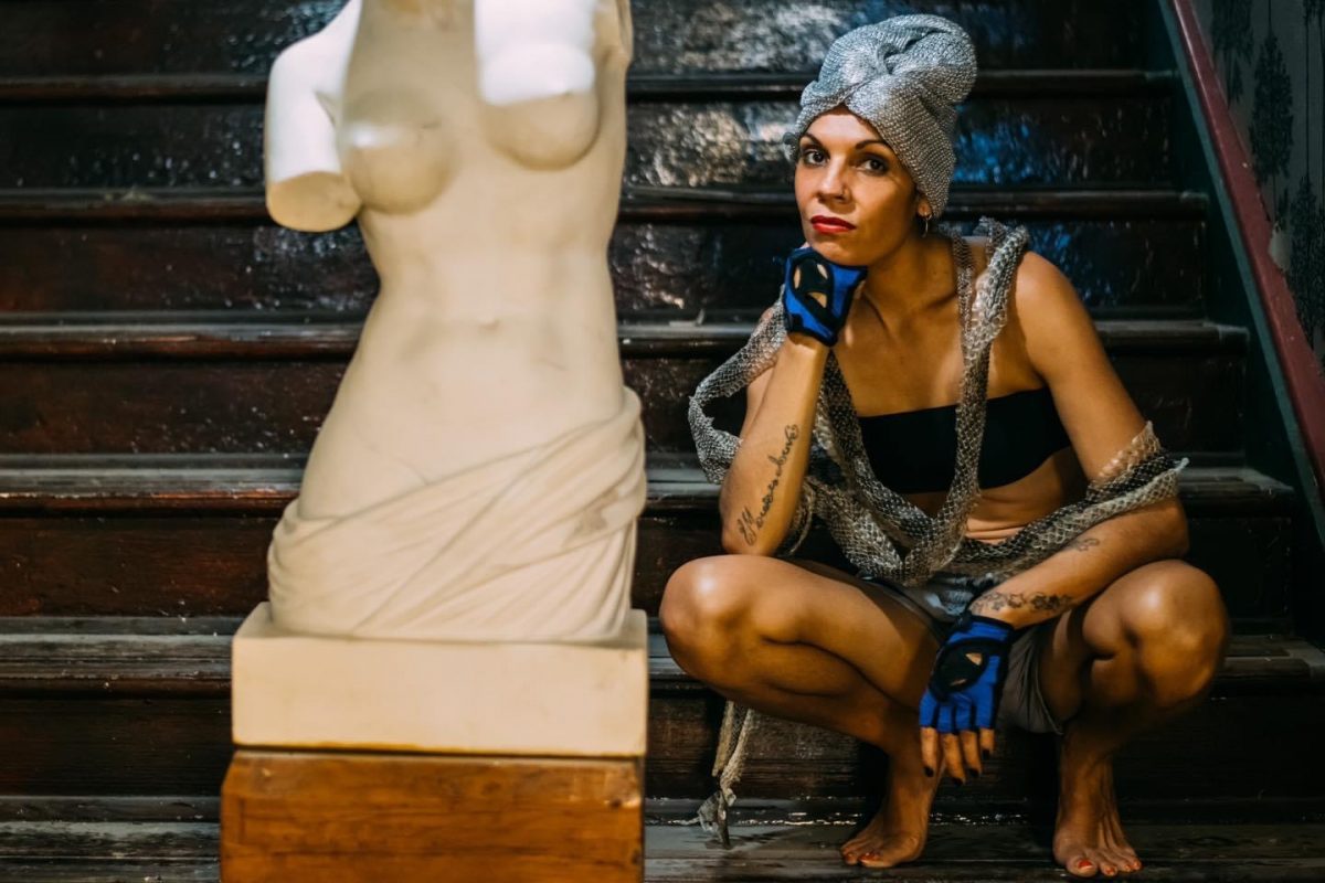 Hip hop artist Dizzy Doolan crouches by a sculpture of a torso