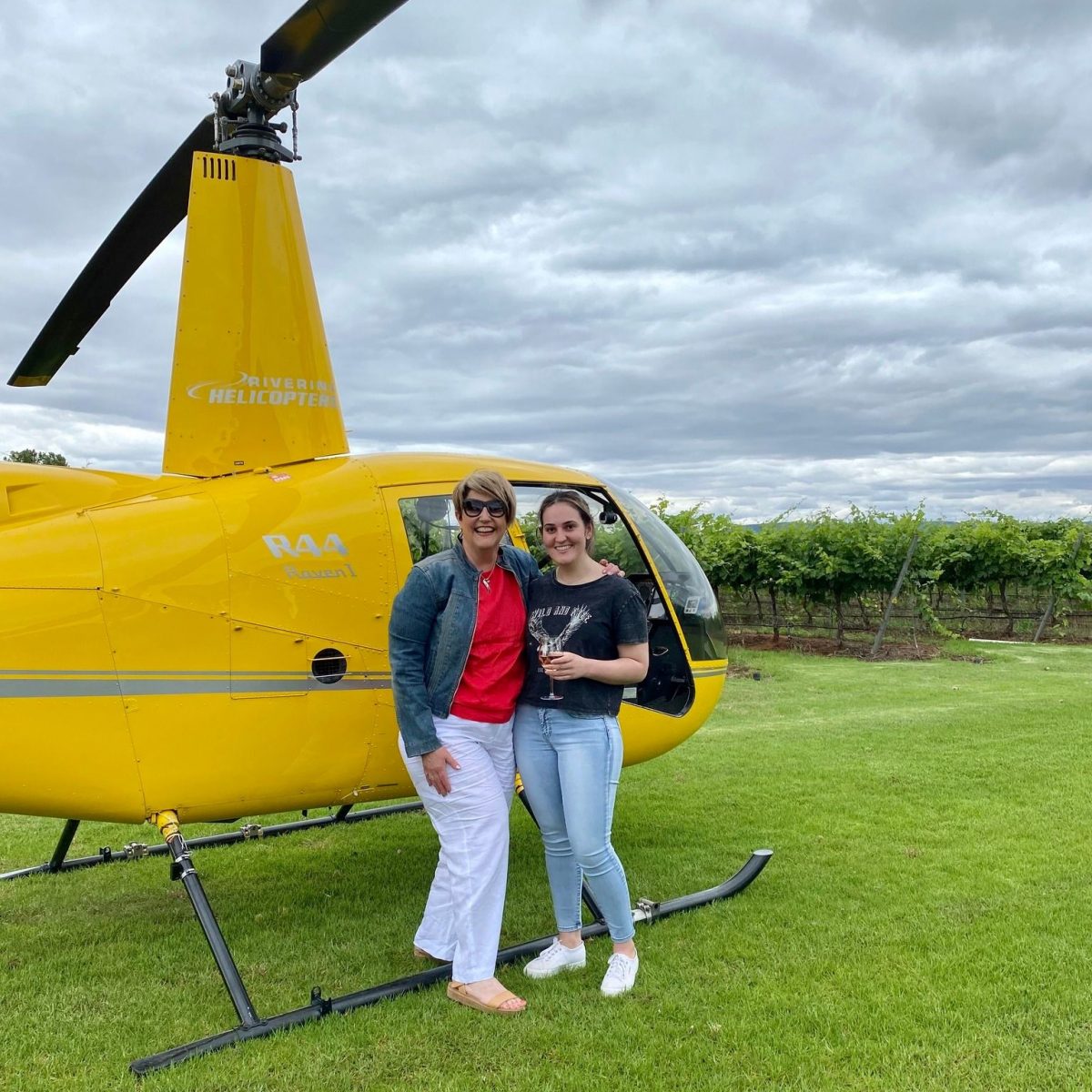 Two women drinking wine in front of helicopter