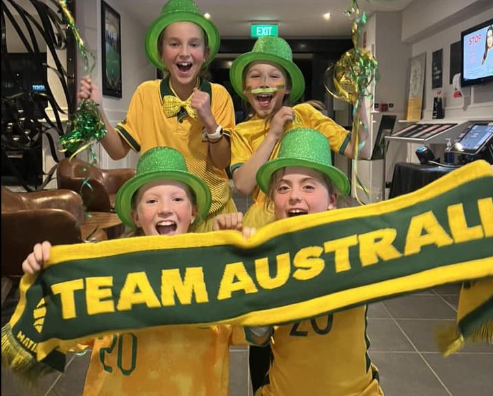 Four girls supporting the Matildas and waving Team Australia football scarf