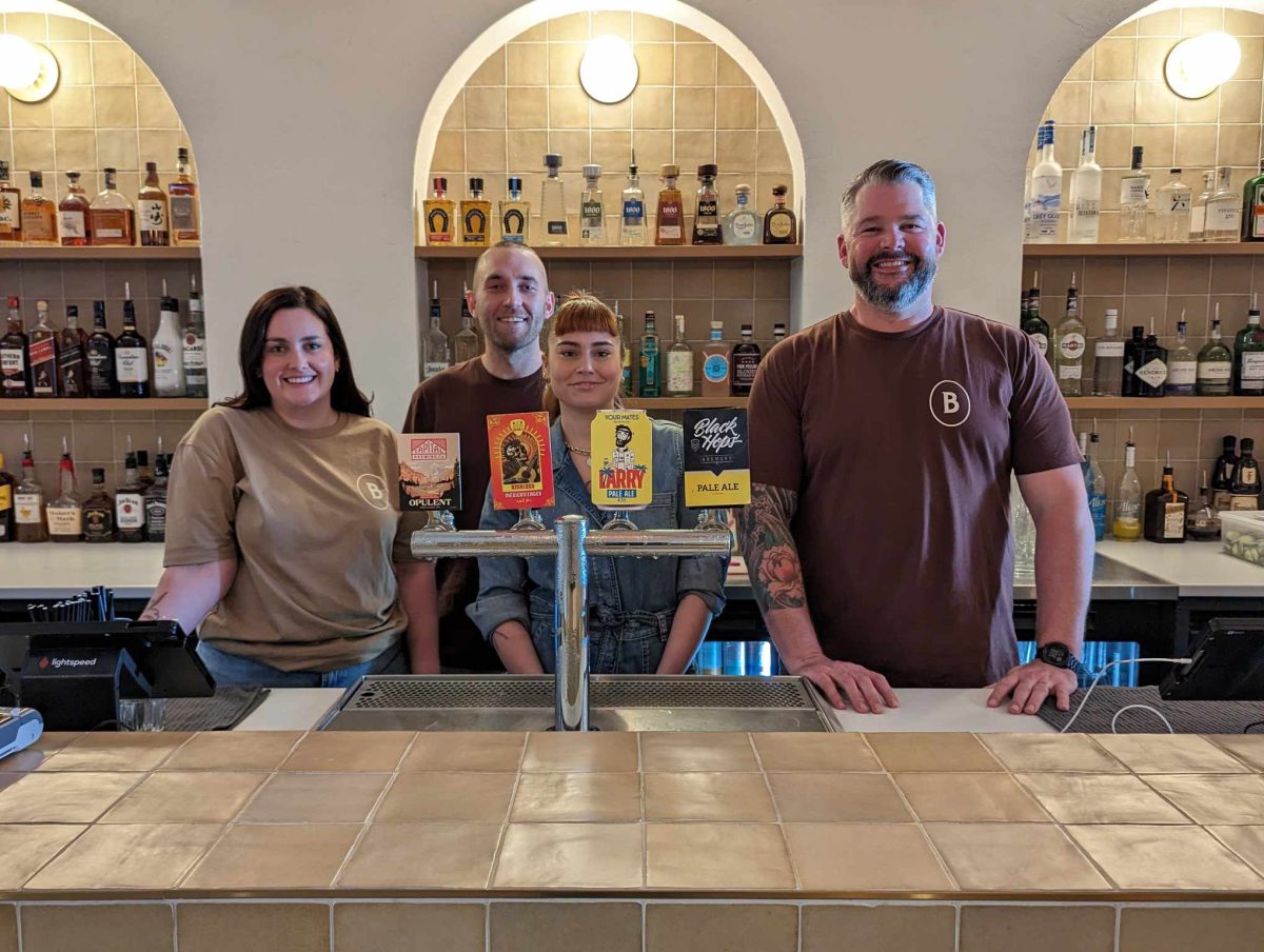 four people standing behind bar