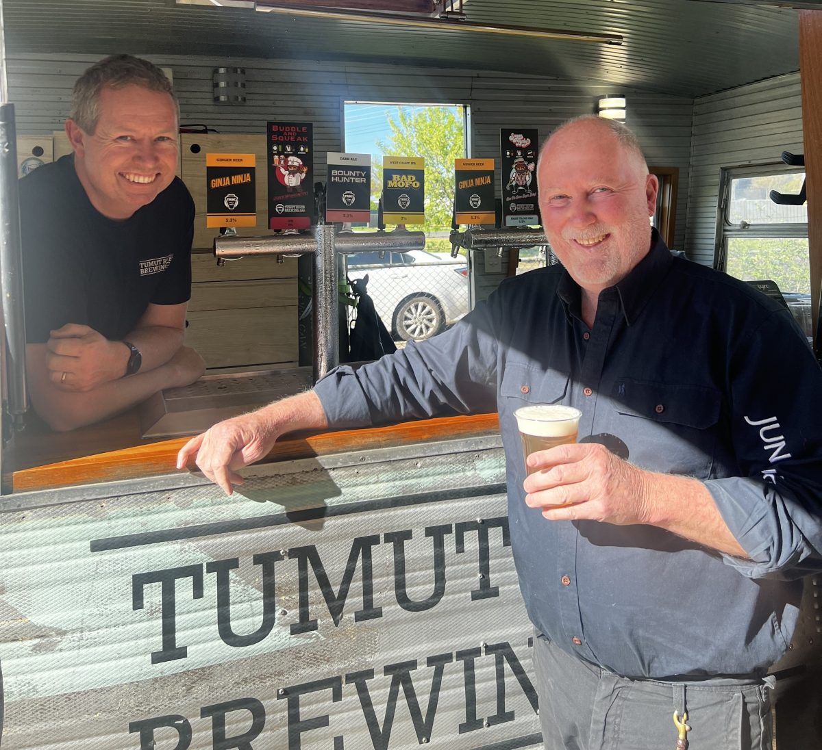 Tim Martin inside the Tumut Brewery truck, and Richard Neale holding a beer outside the front of it. 