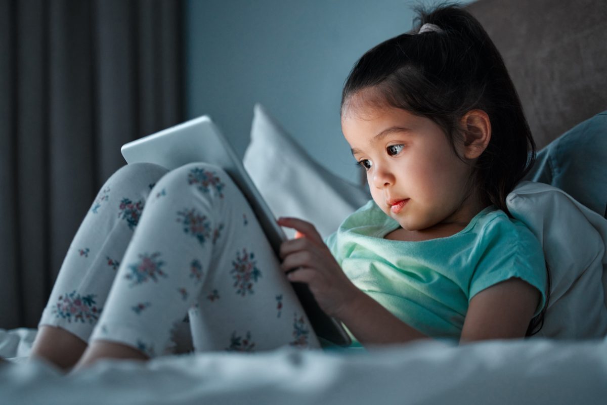 young girl using tablet while lying in bed