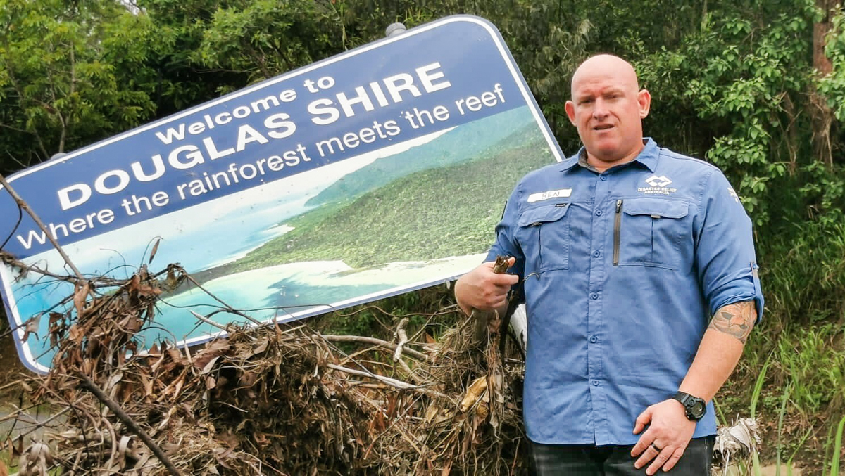 man in blue shirt standing next to a sign damaged by floodwater