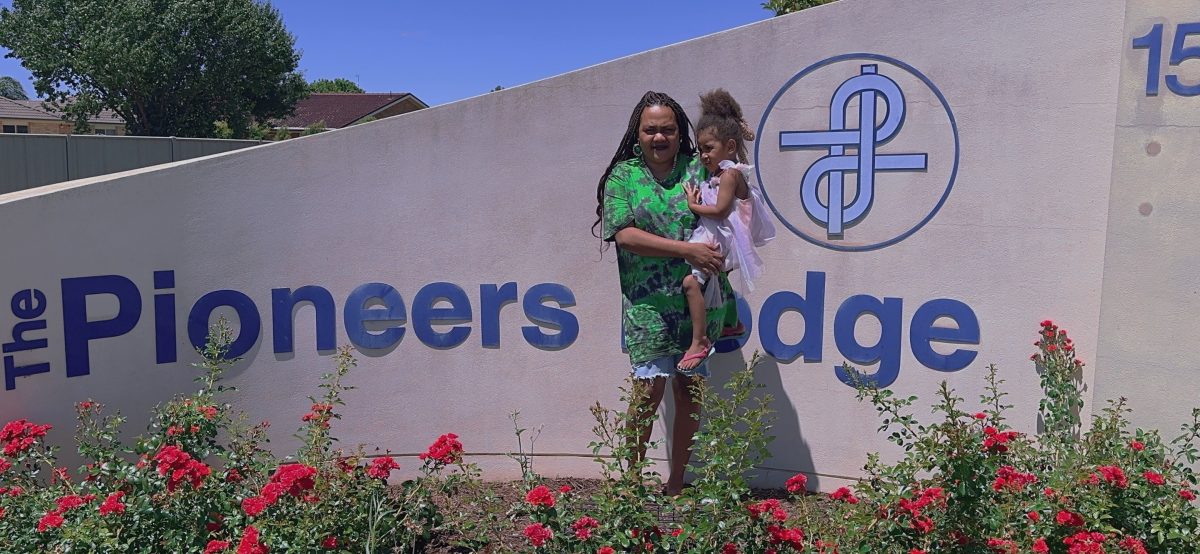 Francina Wilikai holds daughter outside Pioneer Lodge sign 