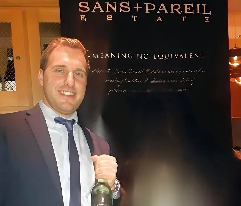 Man holds bottle of wine in front of company sign 