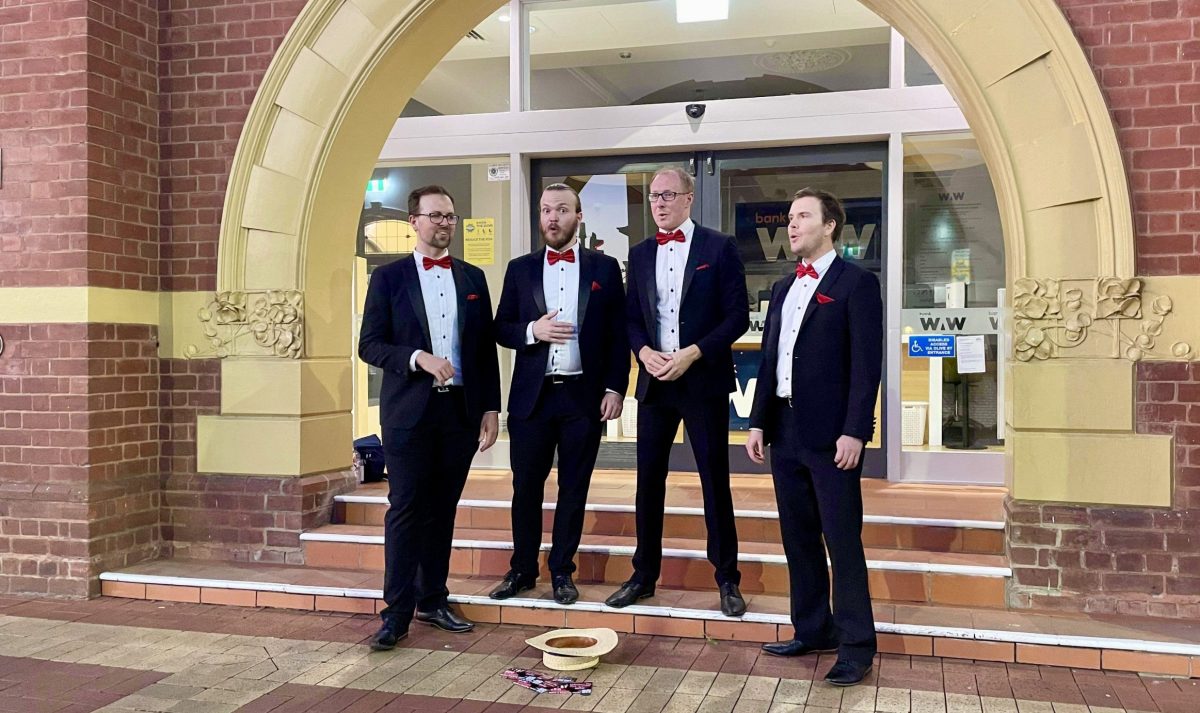 Four men stand on a step singing as a barbershop quartet