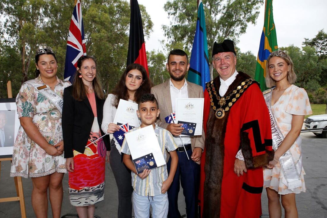 a mayor with two young women wearing sashes, and a family with flags and certificates 