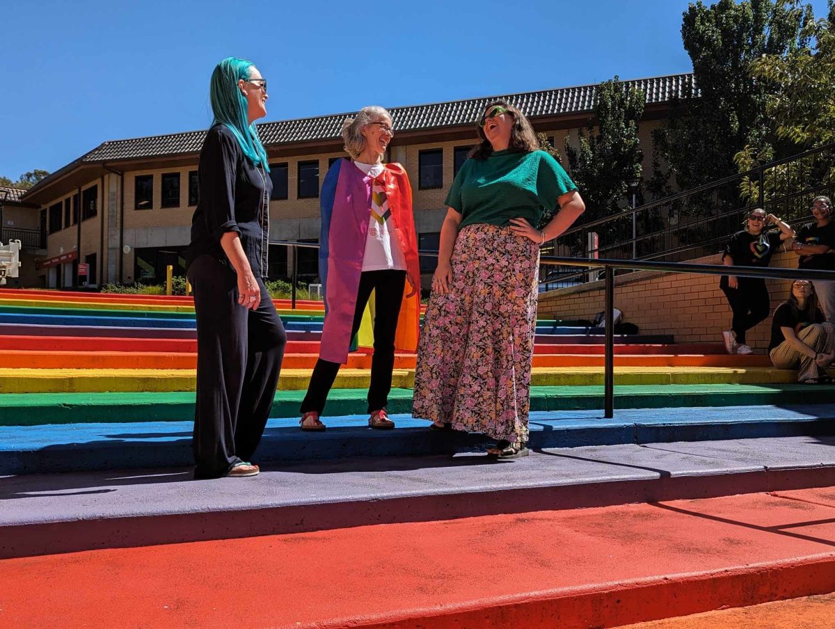 three women standing outside on rainbow-coloured stairs