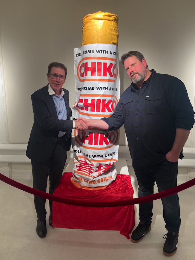 two men and a giant Chiko roll behind a velvet rope