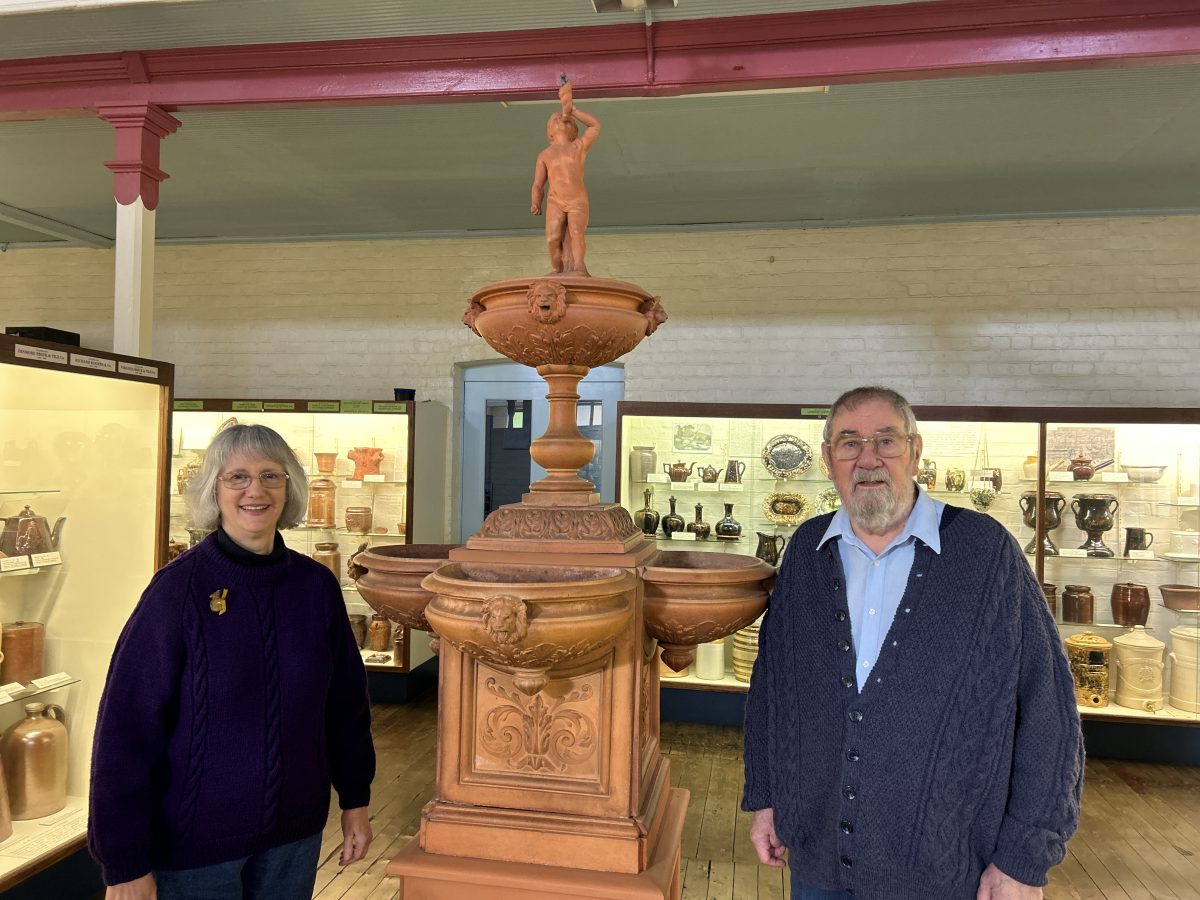 man and woman stand in front of large decorative pottery piece