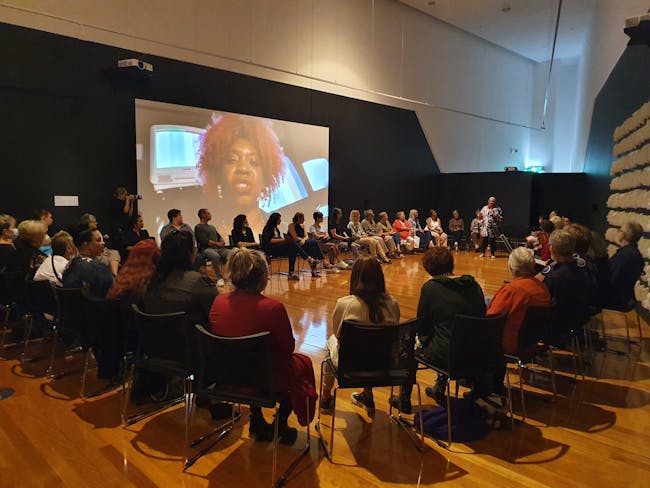 a group of people sitting in chairs in a circle around a woman giving a speech