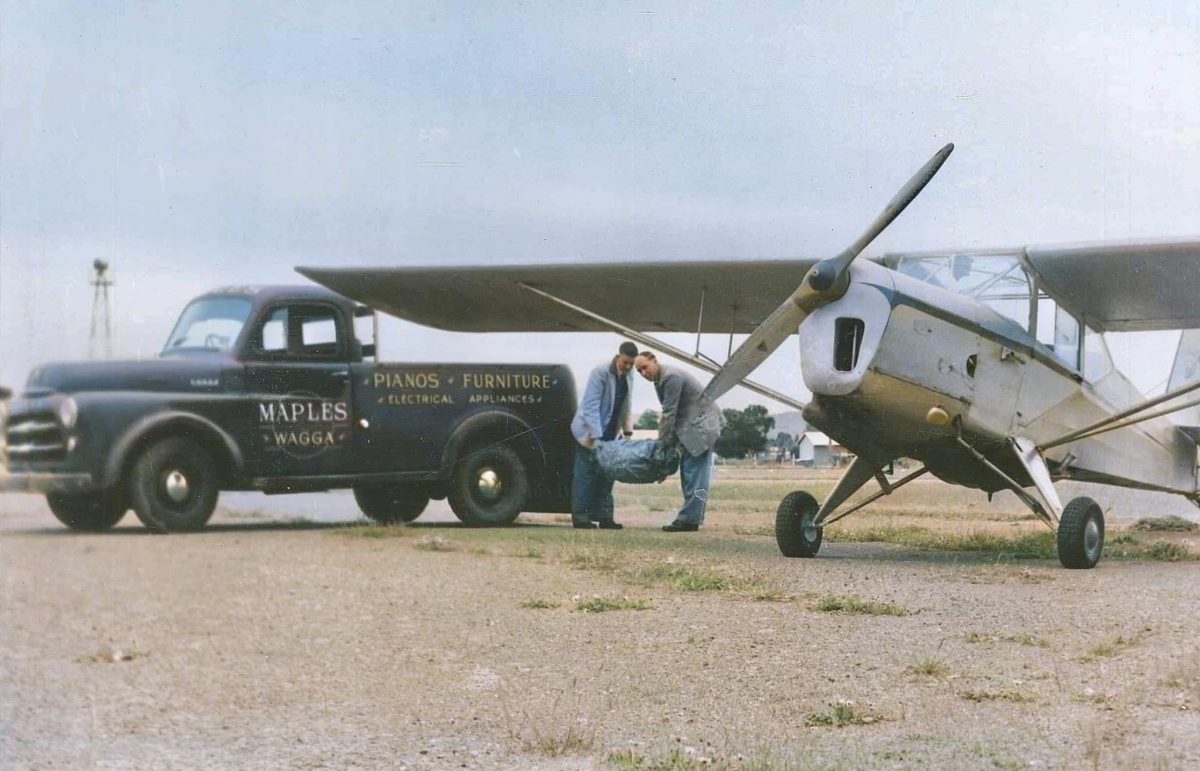 old photo of two men loading a furniture delivery from a ute to a small plane