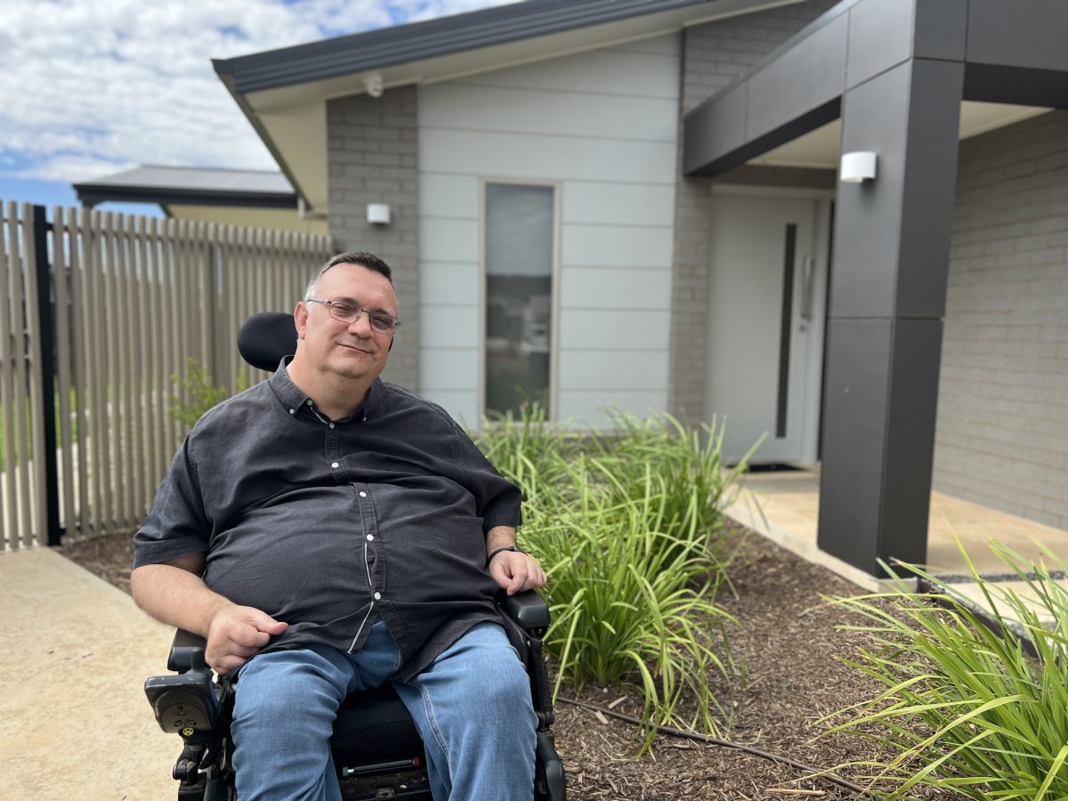 man in wheelchair in front of house