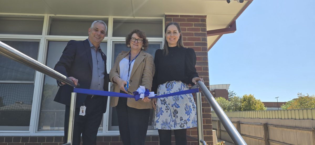 three people cutting a ribbon to mark a building's official opening