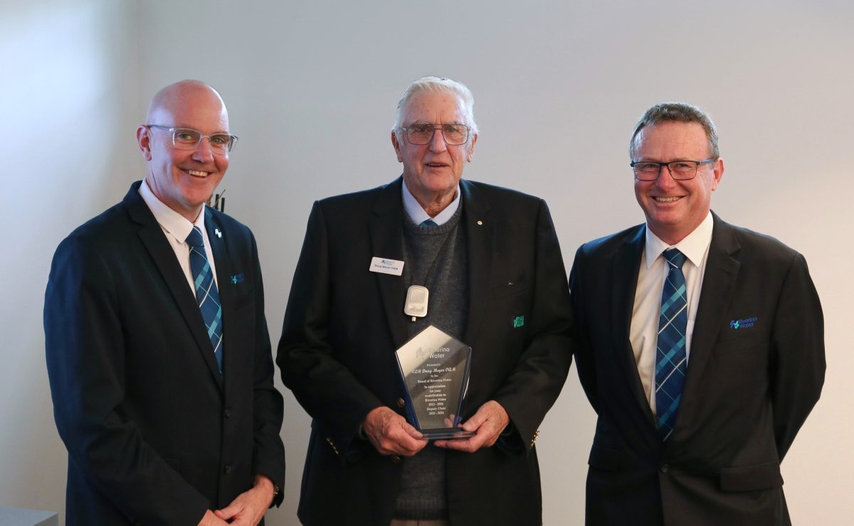 three men in suits, the one in the middle holding an award