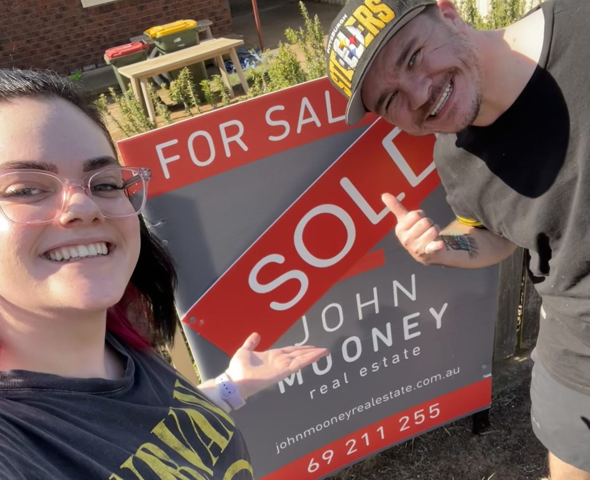 First home buyers stand in front of the SOLD sign at their new property