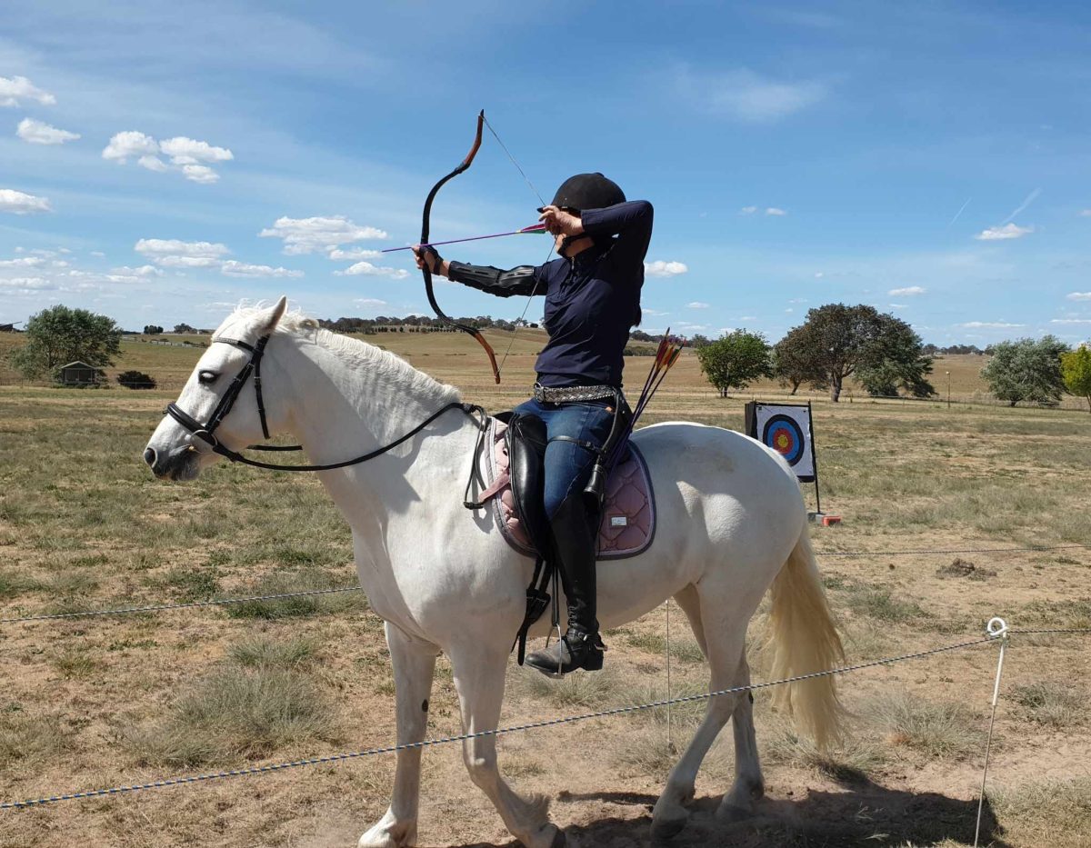 woman shooting with a bow and arrow from horseback 