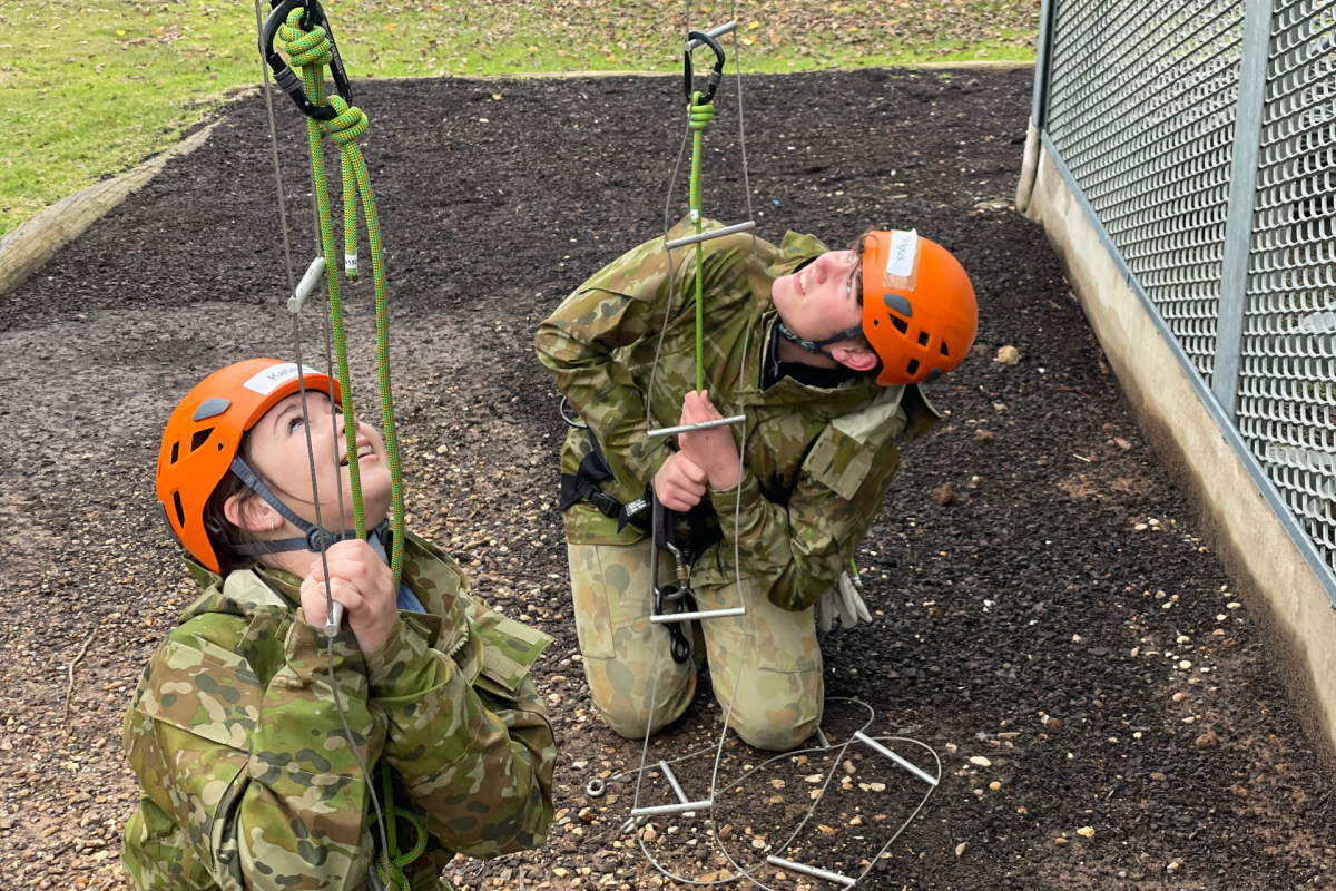 two people kneeling on the ground holding ropes looking upwards