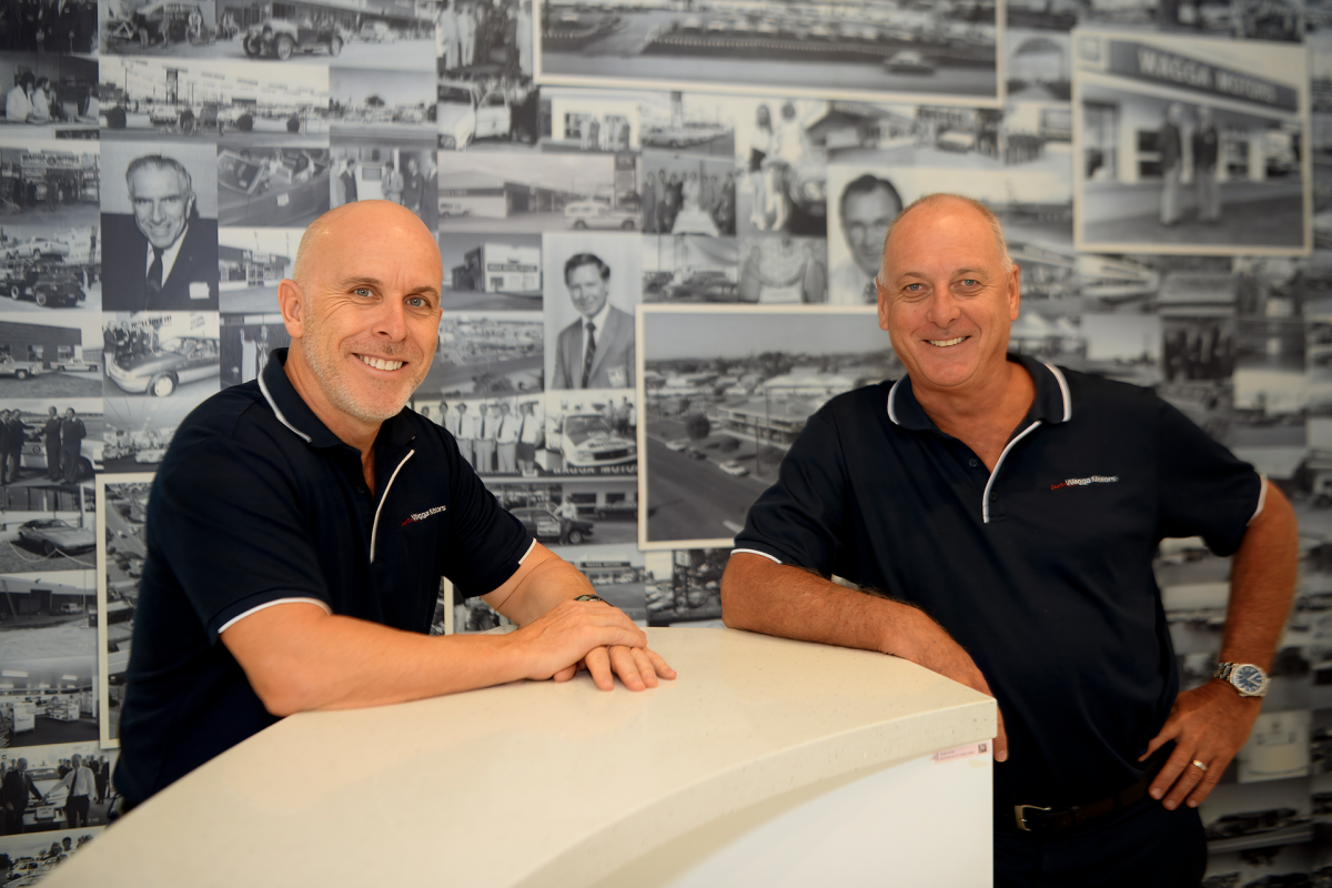 two men standing in the foyer of Wagga Motors with black and white photos behind them