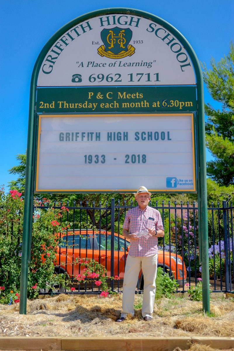 old man in front of school sign 