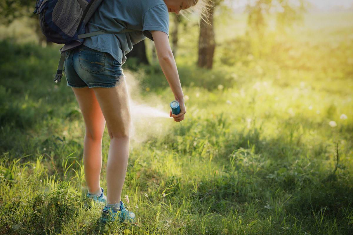 A woman spraying insect repellent on her legs while walking in the bush