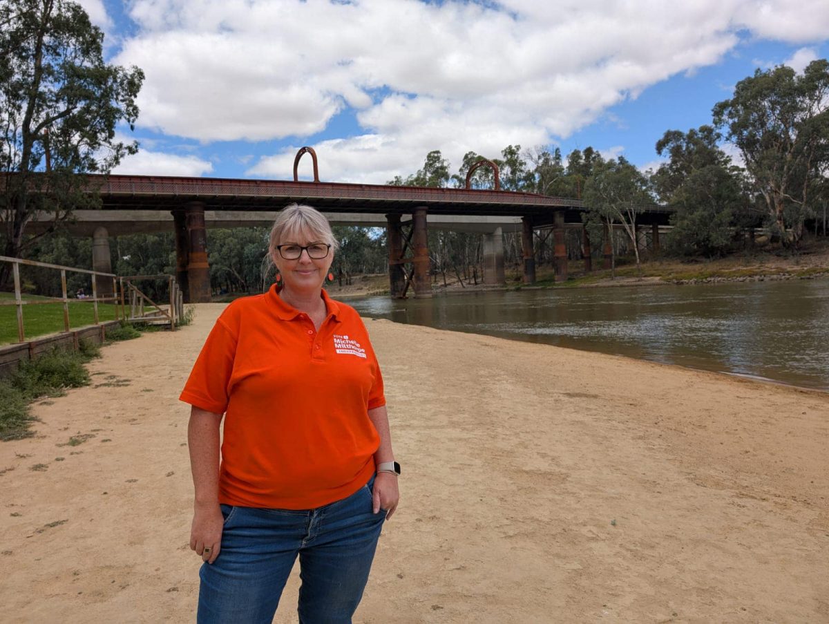 a woman standing on sand near a waterway and bridge 