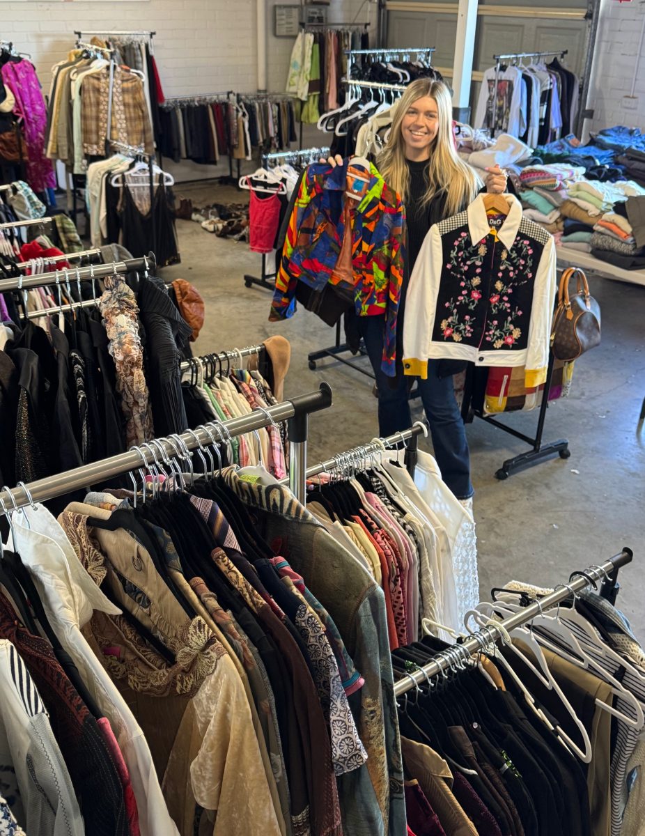 a young woman holding up shirts in a vintage clothing store