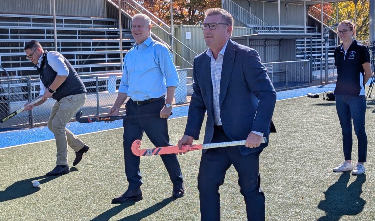 three men with field hockey sticks, with a woman looking on