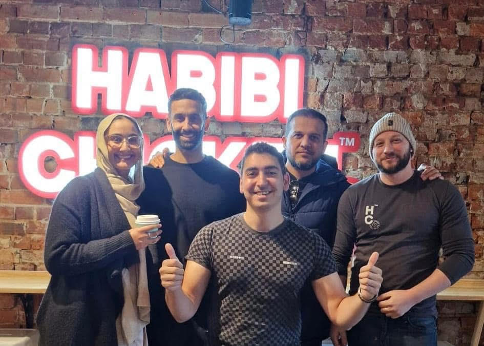 A bunch of happy people in front of the Habibi Chicken sign
