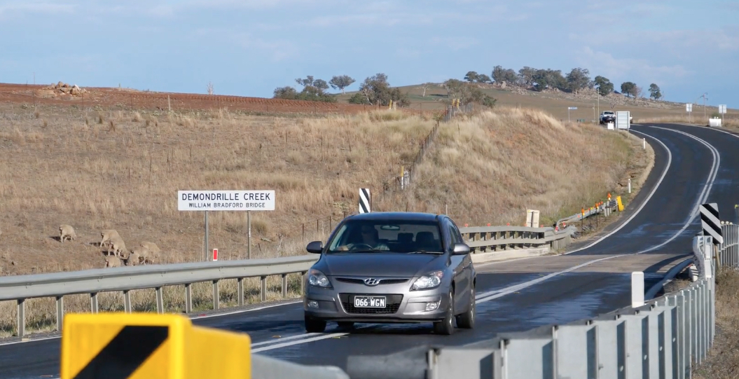 a small silver car on a windy country road with sheep in the background