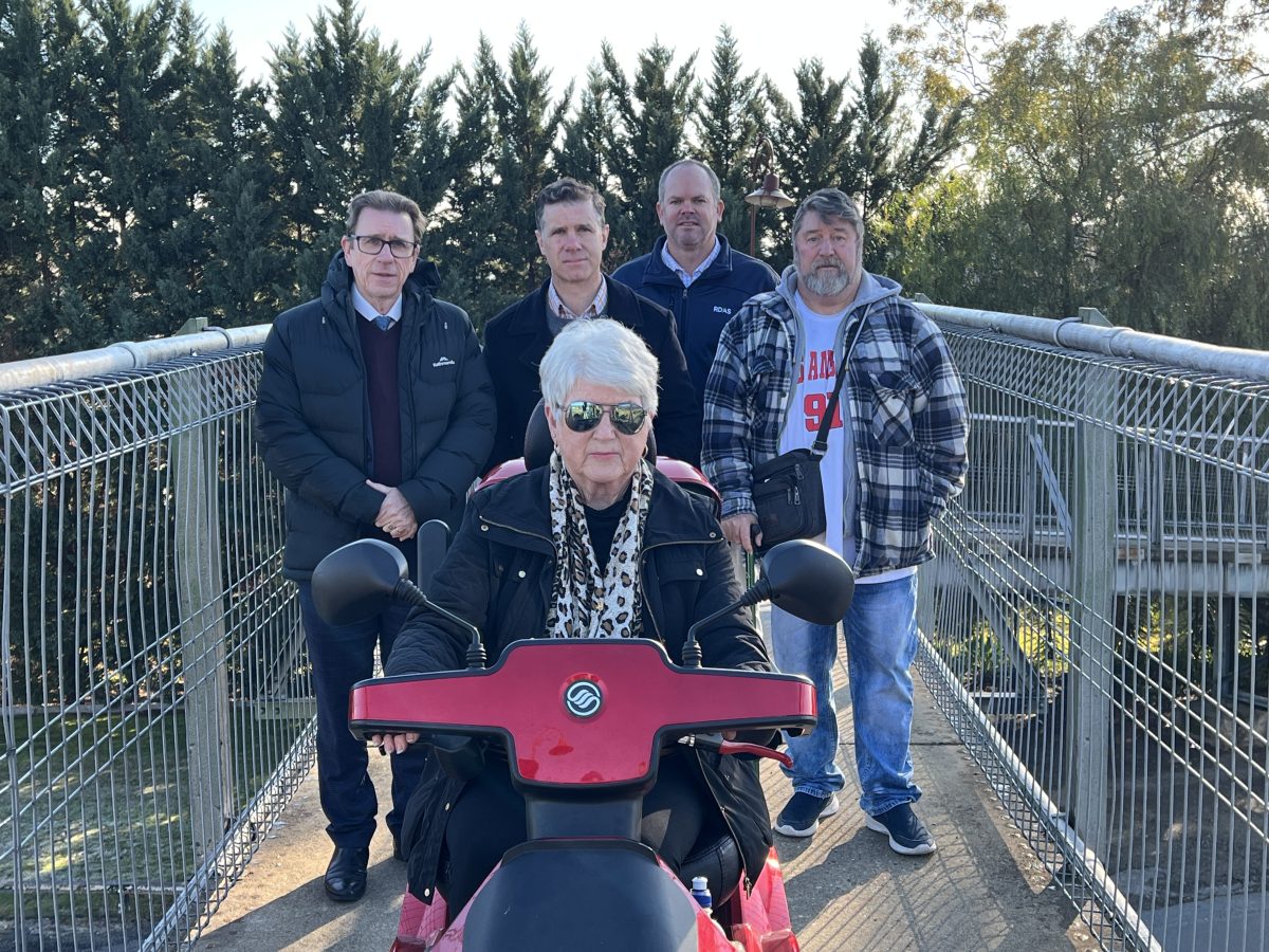 Four men standing behind a woman in a motorised wheelchair on an overpass