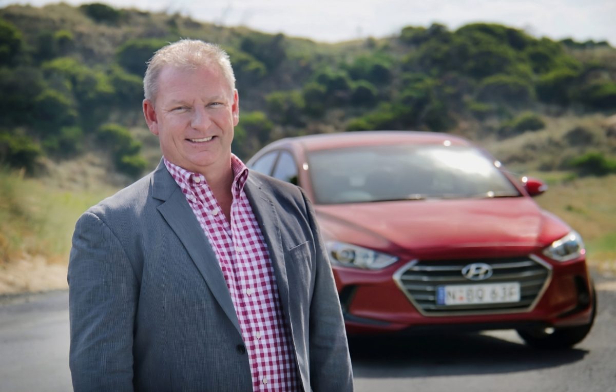 A smiling man standing near a red car