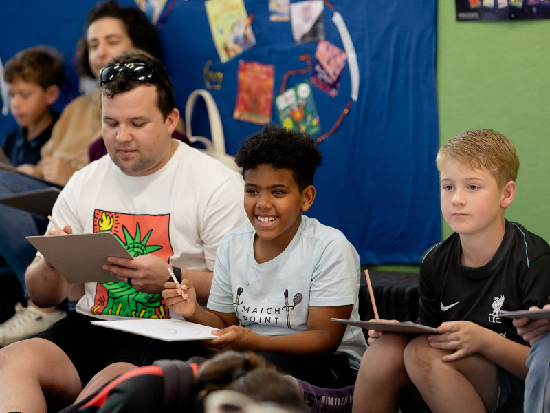 A man and two boys writing while sitting down