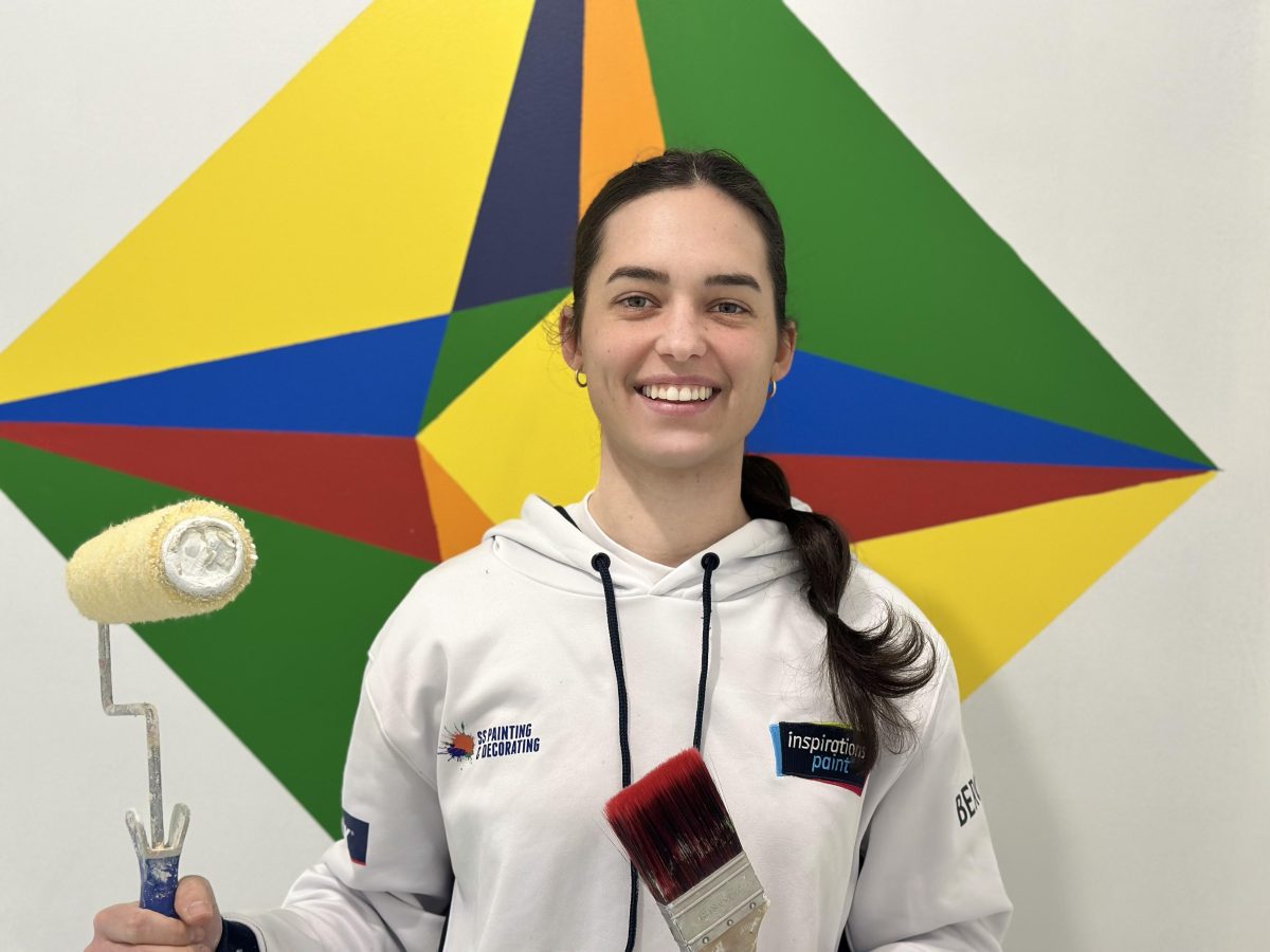 Smiling young woman holding a paint roller and brush