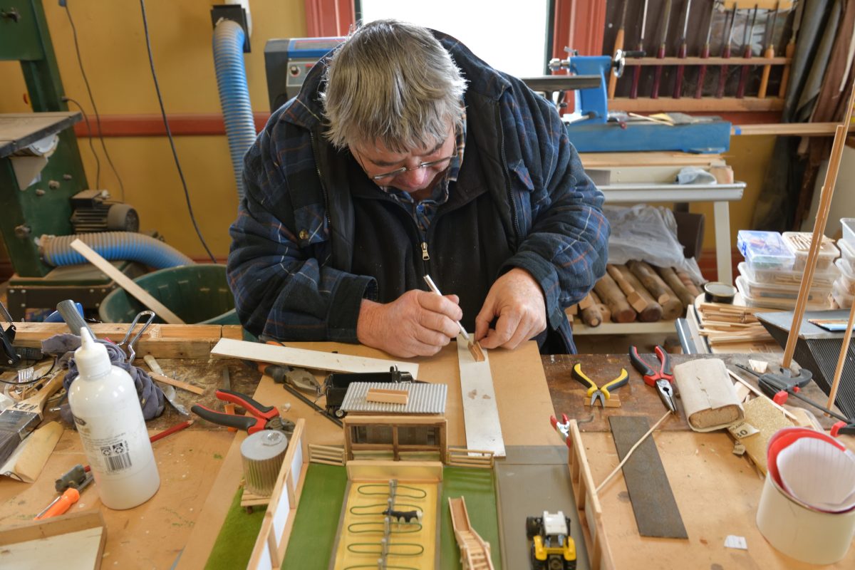 An artist leans over a work bench covered in various materials